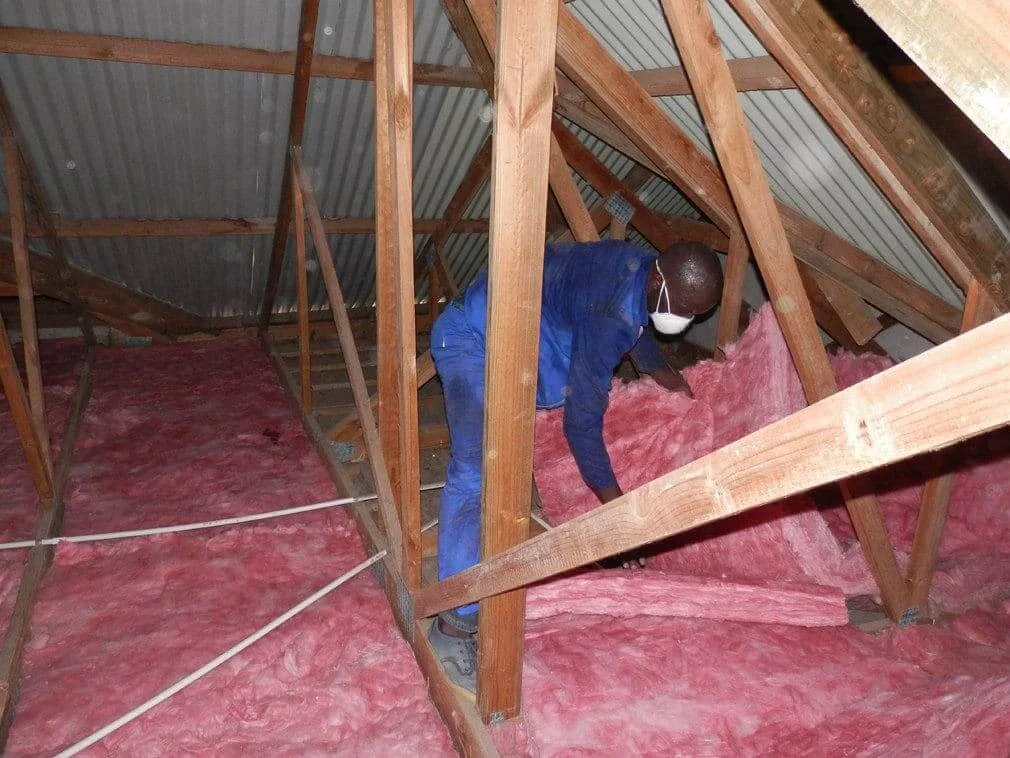 Installer fitting pink insulation between timber roof members